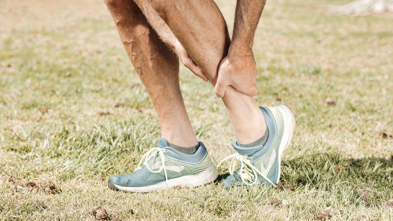 A person in blue sport’s shoes holding their ankle